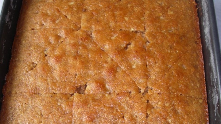 κεικ μελιού Ένα ταψί περιχυμένο με ένα γυαλιστερό, χρυσαφένιο σιρόπι μελιού. Φαίνονται και τα κομματάκια καρυδιού στο εσωτερικό του κέικ.