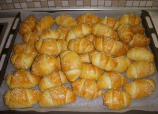 Χρυσαφένια τυροπιτάκια σε σχήμα μικρού κρουασάν, πασπαλισμένα με σουσάμι, τοποθετημένα σε σειρά πάνω σε λαδόκολλα