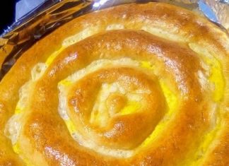 Μια μεγάλη χρυσαφένια κασεροκουλούρα με εμφανή λιωμένα κομμάτια κασεριού στην επιφάνεια τοποθετημένη σε ταψί