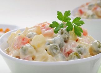 Μια μεγάλη πιατέλα με ρώσικη σαλάτα, διακοσμημένη με αρακά και φέτες καρότου.