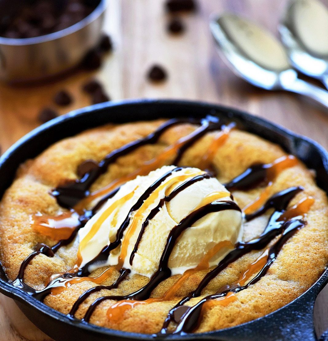 Ένα μικρό, ζεστό κέικ με λιωμένη σοκολάτα, σερβιρισμένο σε ένα πιάτο με μια μπάλα παγωτού βανίλιας από πάνω και περιχυμένο με σιρόπι σοκολάτας και καραμέλας.