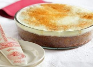 Ένα κομμάτι πολίτικο σιροπιαστό γλυκό με λευκή κρέμα και μπόλικη κανέλα στην κορυφή σερβιρισμένο σε γυάλινο πιάτο