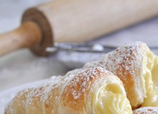 Σειρά από χρυσαφένια τραγανά κορνεδάκια γεμισμένα με πλούσια κίτρινη κρέμα πατισερί και πασπαλισμένα με άχνη ζάχαρη