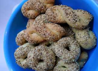 Σειρές από χρυσαφένια κουλουράκια λαδιού πασπαλισμένα με σουσάμι πάνω σε λαδόκολλα, αναδίδοντας αρώματα πορτοκαλιού και κανέλας