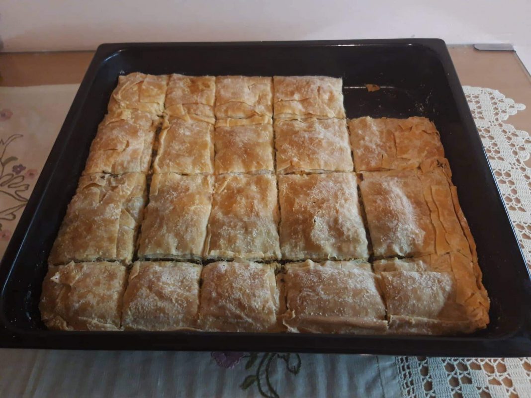 Ένα ταψί χρυσαφένιας, τραγανής σπανακοτυρόπιτας με ορατές στρώσεις φύλλου και πλούσια πράσινη γέμιση.