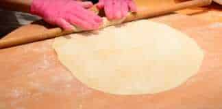 Ζύμη για πίτα, πιασμένη σε μπάλα, σκεπασμένη με πετσέτα για να ξεκουραστεί, μερικές μικρές μπάλες ζύμης δίπλα.