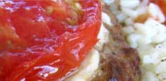 Λαχταριστά μπιφτέκια στο ταψί, καλυμμένα με λιωμένο τυρί και μια φέτα ντομάτας, δίπλα σε φρέσκο μαϊντανό.