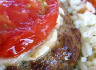 Λαχταριστά μπιφτέκια στο ταψί, καλυμμένα με λιωμένο τυρί και μια φέτα ντομάτας, δίπλα σε φρέσκο μαϊντανό.