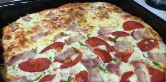 Μια τετράγωνη, ζεστή πίτσα με λιωμένο τυρί, μπέικον, πιπεριές και κόκκινη σάλτσα, έτοιμη να κοπεί.