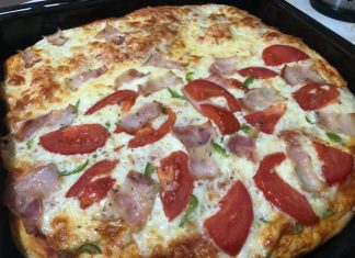 Μια τετράγωνη, ζεστή πίτσα με λιωμένο τυρί, μπέικον, πιπεριές και κόκκινη σάλτσα, έτοιμη να κοπεί.