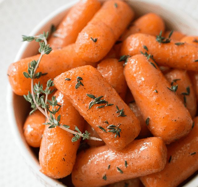 καροτα Ένα μπολ γεμάτο με λαμπερά, πορτοκαλί καρότα baby καλυμμένα με μια σκούρα, γλυκιά σάλτσα.