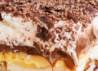 Πολλαπλά στρώματα από το 'Απόλυτο Γλυκό' με βάση καρυδιού, κρέμα τυριού, πουτίγκα και σαντιγί, σερβιρισμένα σε τετράγωνο κομμάτι.