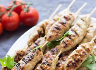 Ψημένα κεμπάπ κοτόπουλου σε ξύλινα σουβλάκια, τοποθετημένα σε πιατέλα, με λαχανικά και σως στο φόντο, έτοιμα για σερβίρισμα.