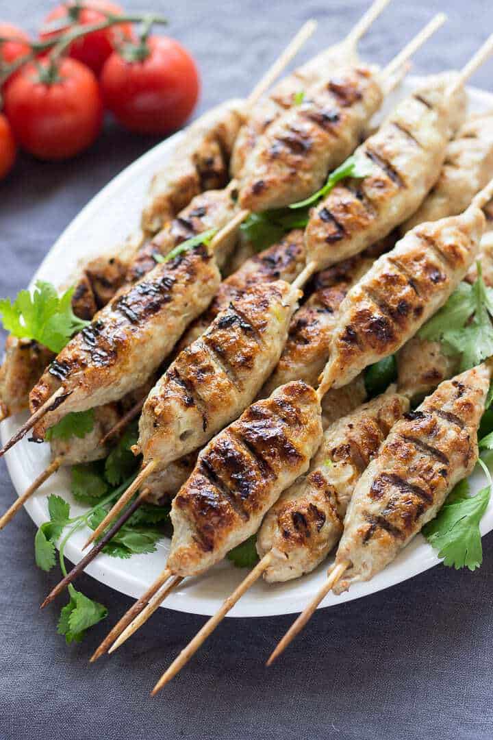 κεμπαπ κοτόπουλο Ψημένα κεμπάπ κοτόπουλου σε ξύλινα σουβλάκια, τοποθετημένα σε πιατέλα, με λαχανικά και σως στο φόντο, έτοιμα για σερβίρισμα.