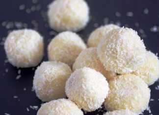 Σπιτικά τρουφάκια Raffaello καλυμμένα με τριμμένη καρύδα, τοποθετημένα σε πιατέλα, με ένα κομμένο στη μέση για να φαίνεται το αμύγδαλο στο κέντρο.