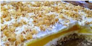 Μια εντυπωσιακή τούρτα λεμονιού σε στρώσεις, με λευκή κρέμα τυριού, κίτρινη λεμονόκρεμα και αφράτη σαντιγί, πασπαλισμένη με λευκή σοκολάτα και καρύδια.