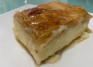 Ένα κομμάτι χρυσαφένιου γαλακτομπούρεκου με εμφανή τα τραγανά φύλλα και το σιρόπι.