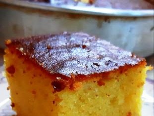 Χρυσαφένια κομμάτια σιροπιασμένης γιαουρτίνης πασπαλισμένα με αμύγδαλα μέσα σε ταψί