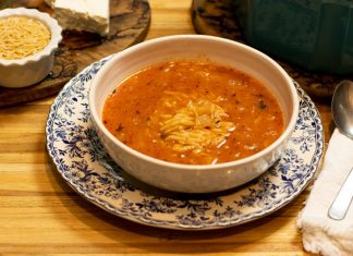 Ένα μπολ με κόκκινη σούπα μανέστρα, με μικρά ζυμαρικά και ψιλοκομμένα μυρωδικά στην επιφάνεια.