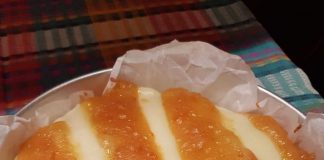 Ένα κομμάτι κέικ με κρεμώδη στρώση στην επιφάνεια και κόκκινες γραμμές από σάλτσα κερασιού ανάμεσά τους, σερβιρισμένο σε λευκό πιάτο.