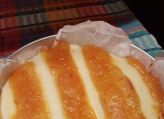 Ένα κομμάτι κέικ με κρεμώδη στρώση στην επιφάνεια και κόκκινες γραμμές από σάλτσα κερασιού ανάμεσά τους, σερβιρισμένο σε λευκό πιάτο.