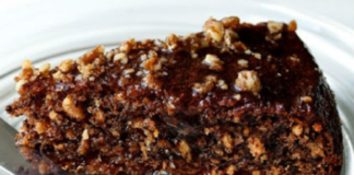 Ένα κομμάτι αγιορείτικης καρυδόπιτας με γλάσο σοκολάτας σε ένα λευκό πιάτο. Φαίνονται τα καρύδια και η σκούρα σοκολάτα στην επιφάνεια.