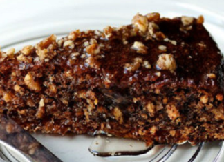 Ένα κομμάτι αγιορείτικης καρυδόπιτας με γλάσο σοκολάτας σε ένα λευκό πιάτο. Φαίνονται τα καρύδια και η σκούρα σοκολάτα στην επιφάνεια.