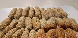 Πιατέλα με χρυσαφένια κουλουράκια λαδιού καλυμμένα με σουσάμι δίπλα σε φρέσκα πορτοκάλια και ξυλάκια κανέλας