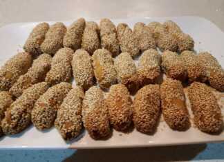 Πιατέλα με χρυσαφένια κουλουράκια λαδιού καλυμμένα με σουσάμι δίπλα σε φρέσκα πορτοκάλια και ξυλάκια κανέλας