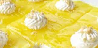 Δροσερό κομμάτι λεμονόπιτας cheesecake σε πιάτο, με εμφανείς τις στρώσεις μπισκότου, λευκής κρέμας τυριού και λαμπερού κίτρινου γλάσου λεμονιού.