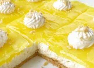 Δροσερό κομμάτι λεμονόπιτας cheesecake σε πιάτο, με εμφανείς τις στρώσεις μπισκότου, λευκής κρέμας τυριού και λαμπερού κίτρινου γλάσου λεμονιού.