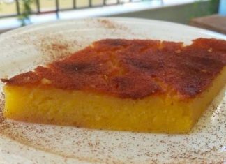 Ένα κομμάτι χρυσαφένιας Λευκαδίτικης γαλατόπιτας με φύλλο, πασπαλισμένη με κανέλα, σε λευκό πιάτο.