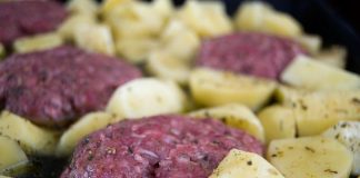 Ένα ταψί με ψημένα, χρυσαφένια μπιφτέκια Σύρου με λιωμένο τυρί στην κορυφή, περιτριγυρισμένα από ψητές πατάτες.