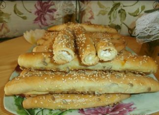 Τραγανά τυροκριτσίνια σε σχήμα ρολού ή πλεξούδας, πασπαλισμένα με σουσάμι και ηλιόσπορους, τοποθετημένα σε ταψί με χαρτί ψησίματος.