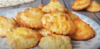 Χρυσαφένια φοντανάκια καρύδας τοποθετημένα σε σειρά πάνω σε λαδόκολλα, με έντονη την υφή της τριμμένης καρύδας στην επιφάνεια