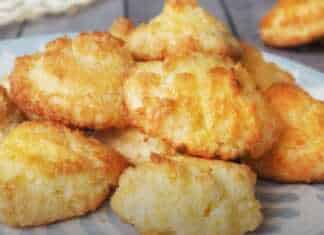 Χρυσαφένια φοντανάκια καρύδας τοποθετημένα σε σειρά πάνω σε λαδόκολλα, με έντονη την υφή της τριμμένης καρύδας στην επιφάνεια