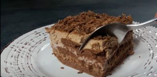 Ένα κομμάτι από γλυκό ψυγείου με στρώσεις σοκολατένιων μπισκότων και κρεμών σοκολάτας και μπισκότου, πασπαλισμένο με τριμμένη κουβερτούρα, σε λευκό πιάτο.