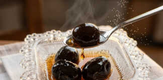 Μαύρα γυαλιστερά καρυδάκια μέσα σε πυκνό σιρόπι, αρωματισμένα με ξυλάκια κανέλας και γαρύφαλλο μέσα σε γυάλινο βάζο