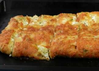 Ένα ψημένο κολοκυθοτυρόψωμο με χρυσαφένια κρούστα, κομμένο σε λωρίδες, με τριμμένο τυρί στην επιφάνεια.