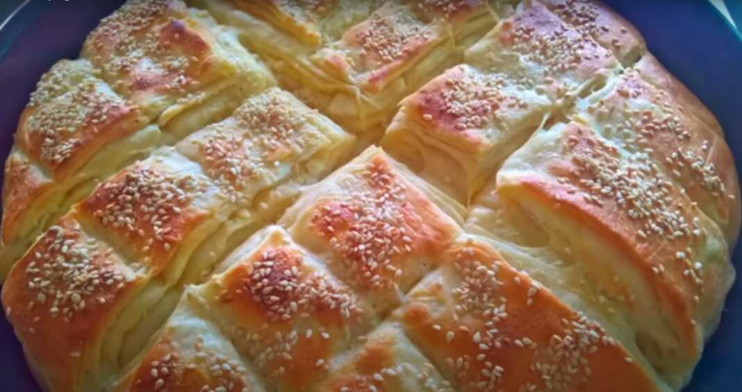 Χρυσαφένιο και αφράτο πιτοτυρόψωμο στο ταψί με εμφανείς τις στρώσεις ζύμης πασπαλισμένο με μπόλικο σουσάμι