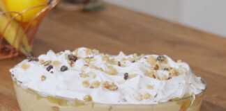 Ένα πυρεξ από γλυκό ψυγείου με στρώσεις κρέμας, μπισκότων σαβαγιάρ, κομμάτια ανανά και μαρέγκα στην κορυφή, πασπαλισμένο με τριμμένο καρύδι και σταφίδες.