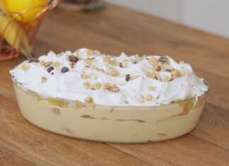 Ένα πυρεξ από γλυκό ψυγείου με στρώσεις κρέμας, μπισκότων σαβαγιάρ, κομμάτια ανανά και μαρέγκα στην κορυφή, πασπαλισμένο με τριμμένο καρύδι και σταφίδες.