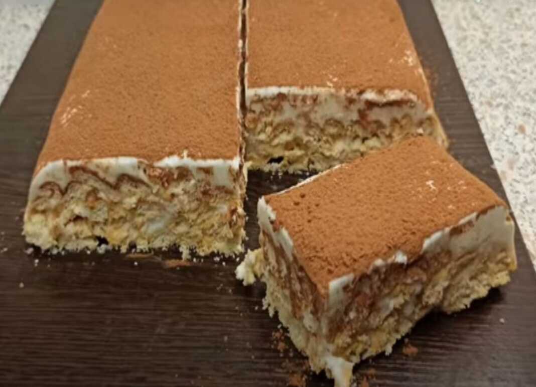 Ένα κομμάτι από γλυκό ψυγείου με γιαούρτι και σπασμένα μπισκότα, πασπαλισμένο με κακάο, σε ένα πιάτο.