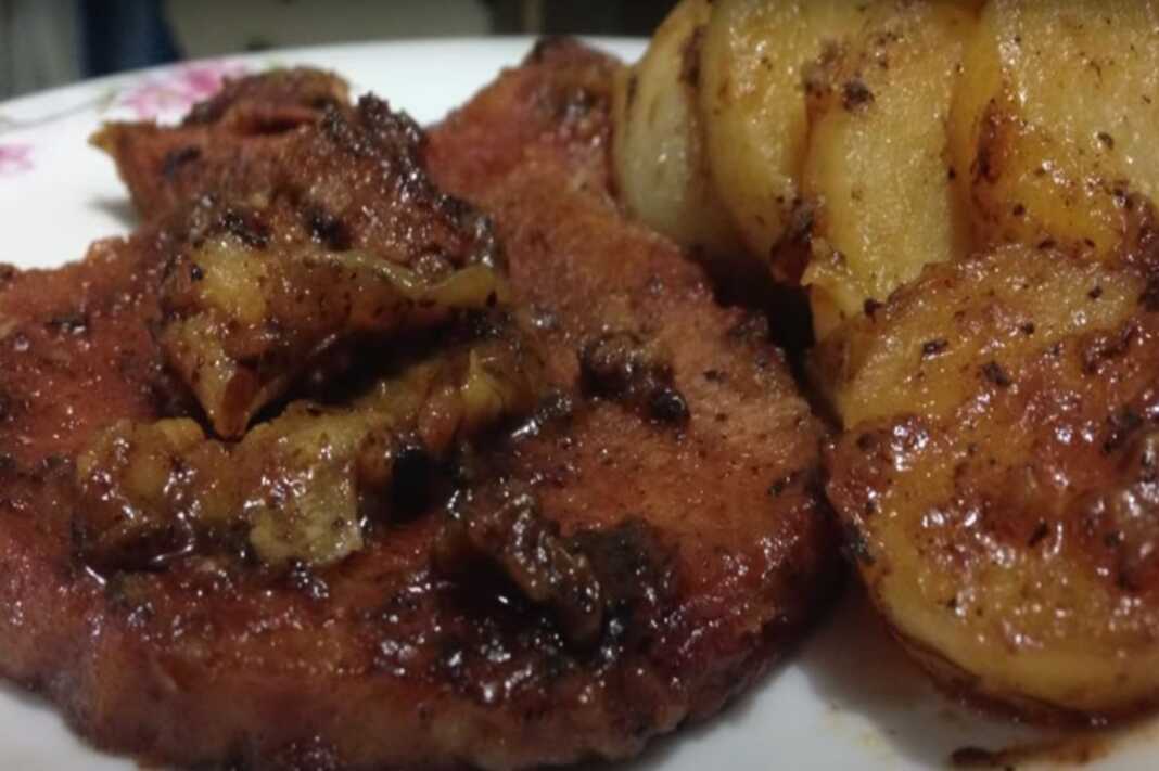 Πιάτο με μελωμένες χοιρινές μπριζόλες στο τηγάνι με πατάτες και πλούσια σάλτσα.