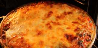 Ένα πυρέξ με στρώσεις από φέτες πατάτας, κιμά και κόκκινη σάλτσα ντομάτας, καλυμμένο με λιωμένο κίτρινο τυρί και λίγο πράσινο μαϊντανό.