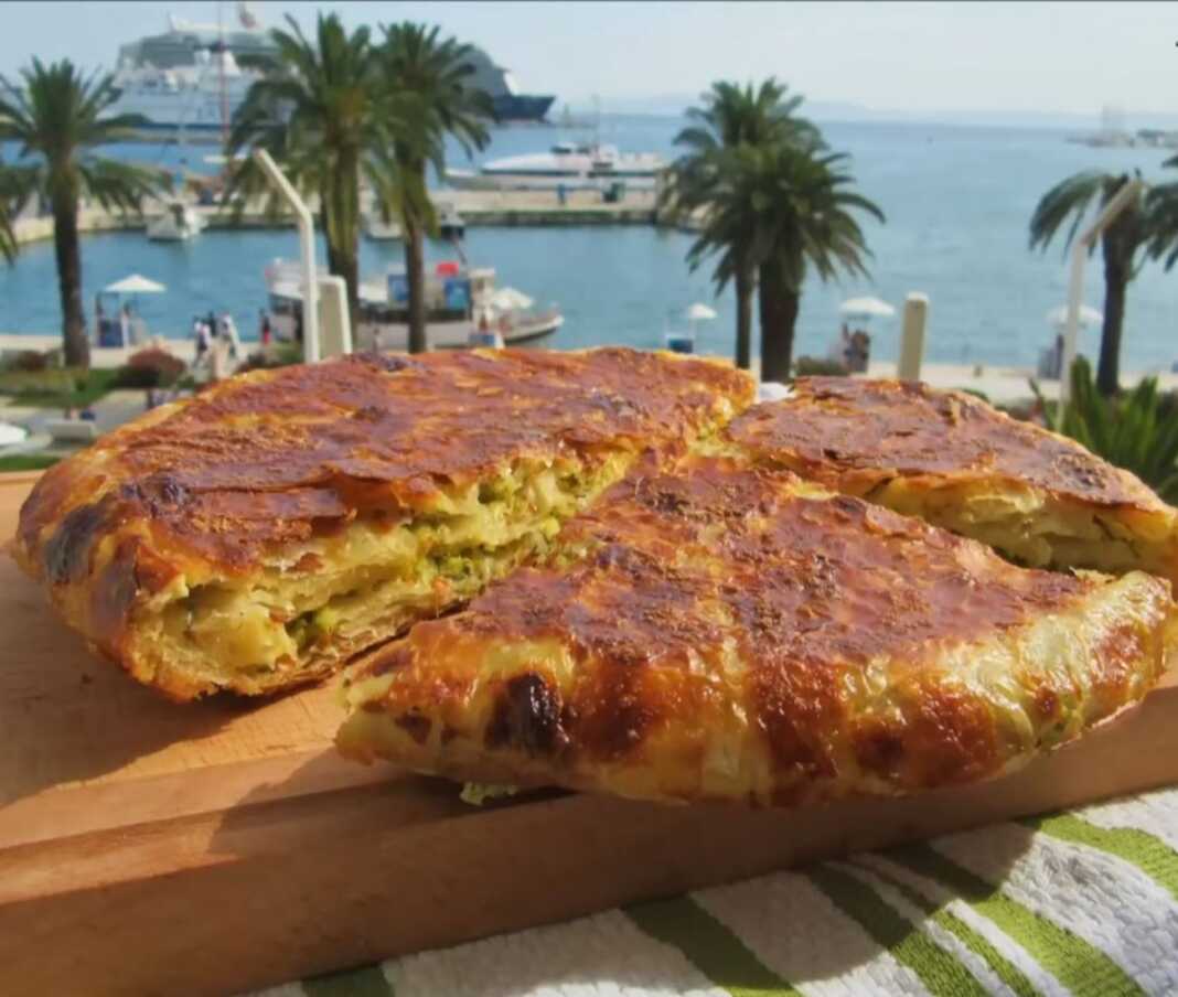 Μια χρυσαφένια, στρογγυλή κολοκυθόπιτα μέσα σε ένα αντικολλητικό τηγάνι, με την επιφάνειά της ελαφρώς ροδισμένη και τραγανή.