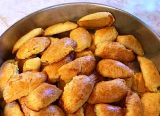 Σειρές από χρυσαφένια τυροπιτάκια κουρού σε σχήμα μισοφέγγαρου, με σχέδια από πιρούνι στις άκρες, πάνω σε αντικολλητικό χαρτί ψησίματος.