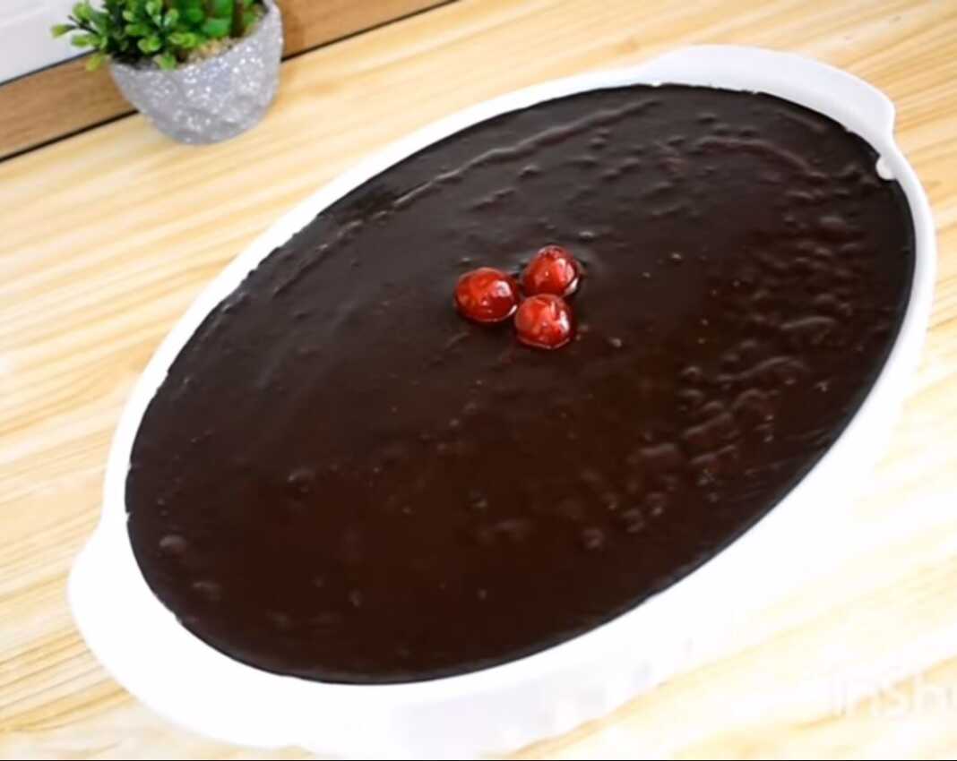 Ένα οβάλ πυρέξ που περιέχει ένα γλυκό σοκολάτας με τρεις στρώσεις: σκούρα σοκολάτα κάτω, λευκή σαντιγί στη μέση και γυαλιστερό γλάσο σοκολάτας στην κορυφή, διακοσμημένο με κόκκινα κερασάκια.