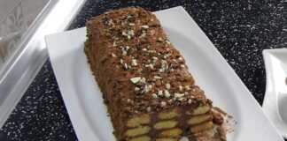 Κορμός Σοκολάτας με σαβαγιάρ Ένας ολόκληρος σοκολατένιος κορμός με σαβαγιάρ σε μια λευκή πιατέλα, πασπαλισμένος με τριμμένη σοκολάτα ή ξηρούς καρπούς.