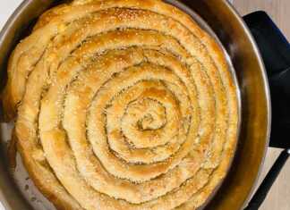 Χρυσαφένια στριφτή τυρόπιτα σε σχήμα σαλιγκαριού μέσα στο ταψί πασπαλισμένη με σουσάμι και τραγανό φύλλο